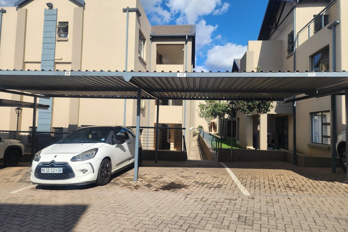 A covered carport area with paved driveway and steel structure located within an apartment complex.