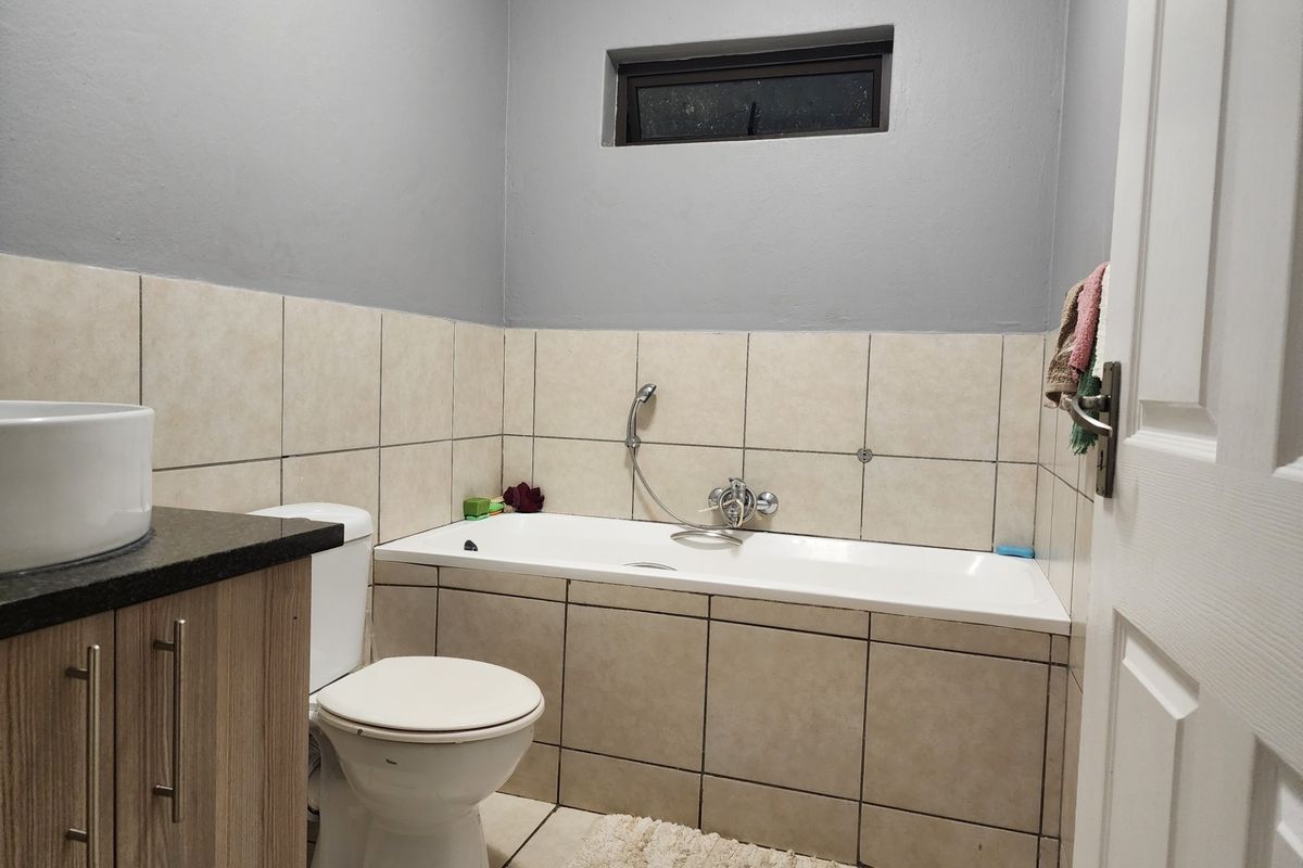 A functional bathroom featuring a built-in vanity with granite countertop, vessel sink, toilet, and a tiled bathtub with a handheld shower mixer.