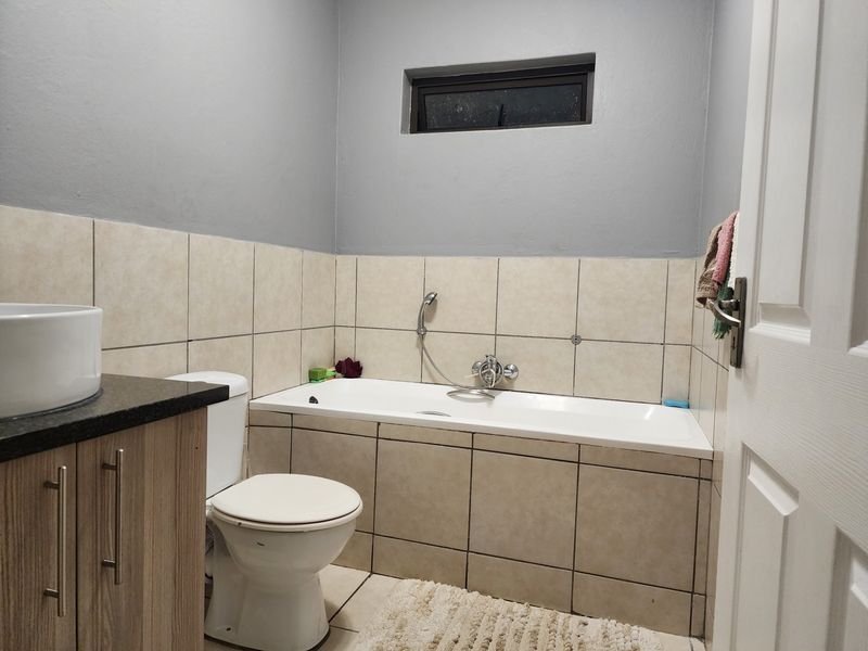A functional bathroom featuring a built-in vanity with granite countertop, vessel sink, toilet, and a tiled bathtub with a handheld shower mixer.