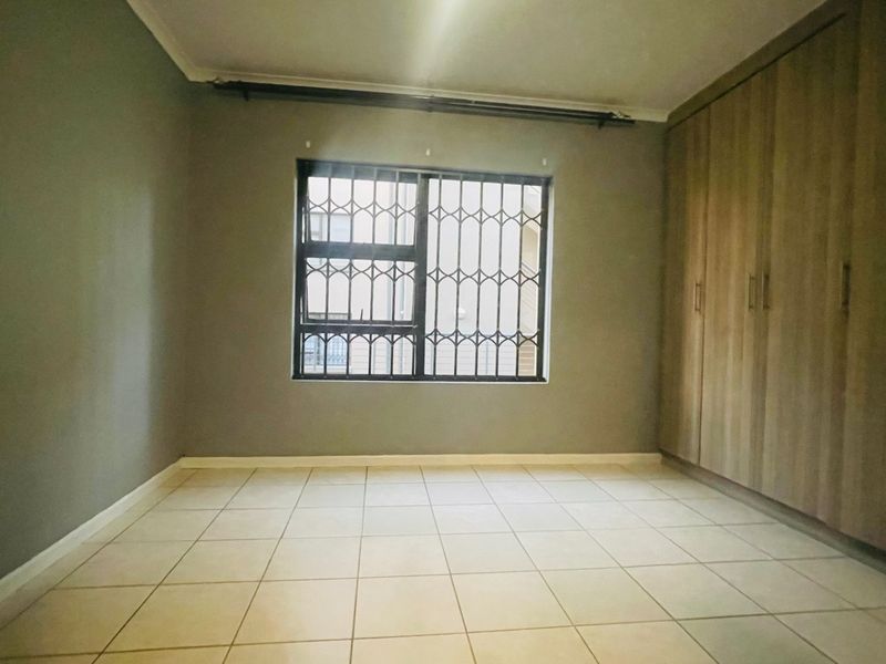 A vacant bedroom featuring neutral wall tones, tiled flooring, and built-in wooden cupboards with a security gate on the window.