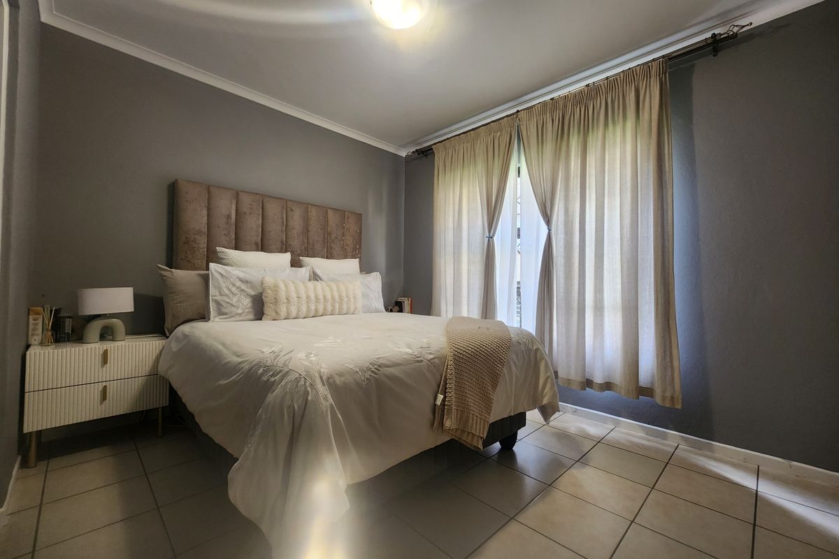 A well-maintained bedroom featuring neutral tiled flooring, grey painted walls, and large windows dressed with floor-to-ceiling curtains.
