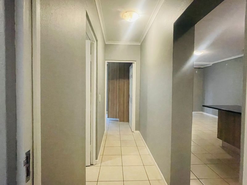 A clean, neutral-toned hallway featuring tiled flooring and access to adjacent living areas and built-in storage.