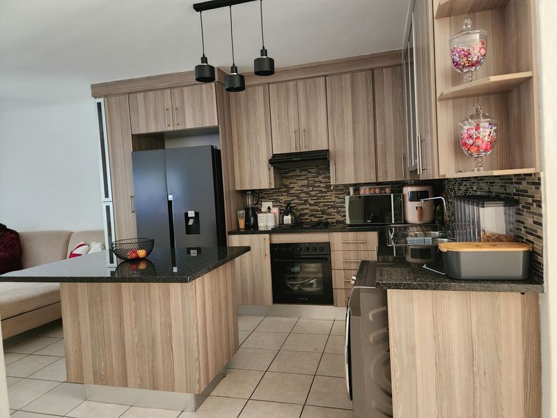 Modern open-plan kitchen featuring wood-grain cabinetry, granite countertops, mosaic backsplash, and a functional island, seamlessly integrated with the adjacent living area.