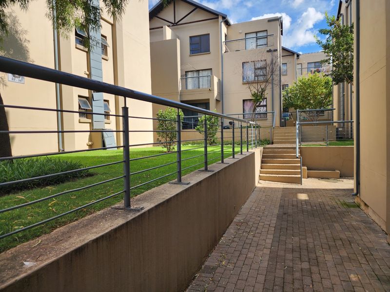 Exterior view of the apartment complex featuring a paved walkway, concrete stairs, and a landscaped lawn area with metal balustrades.