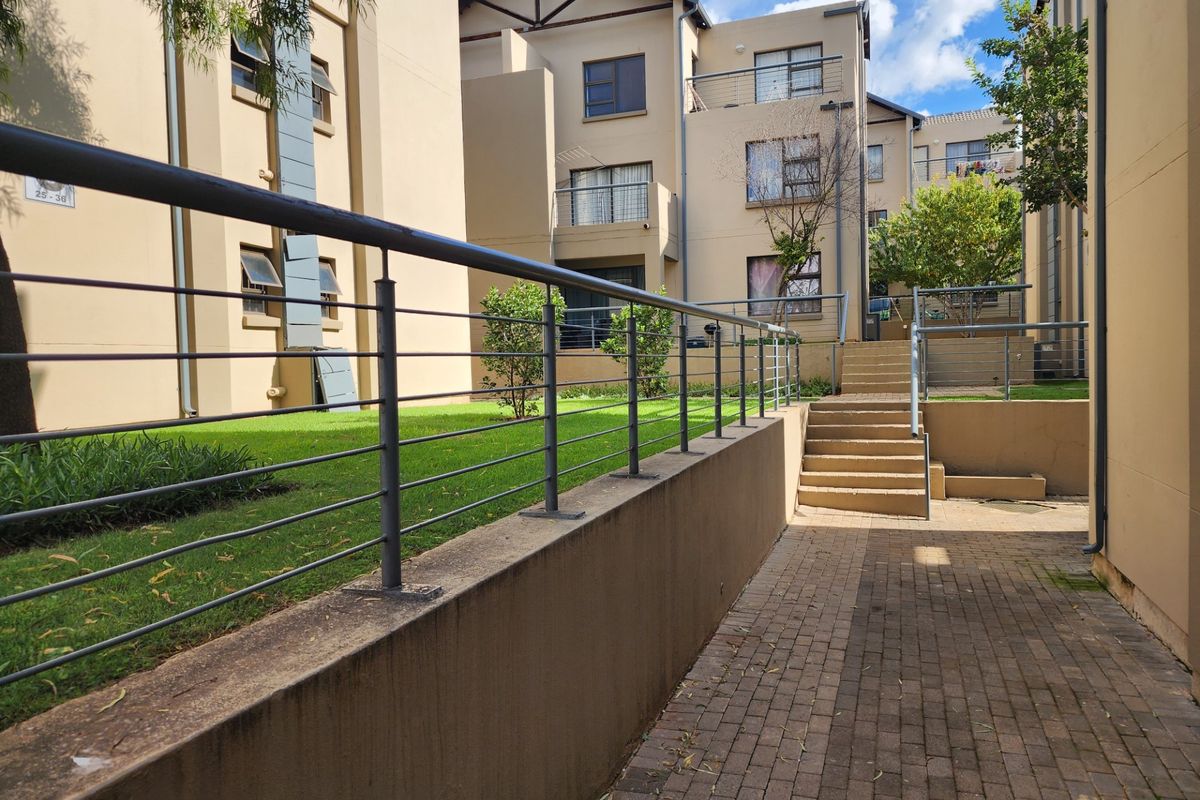 Exterior view of the apartment complex featuring a paved walkway, concrete stairs, and a landscaped lawn area with metal balustrades.