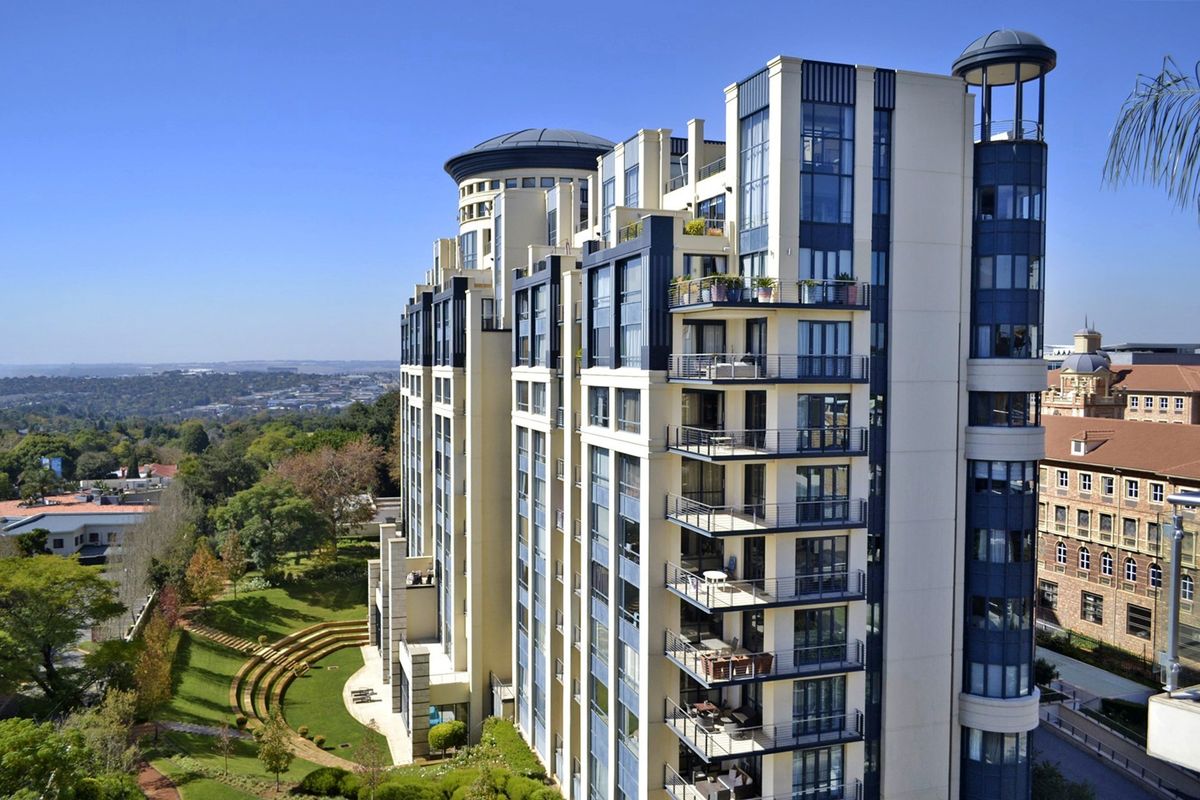 Aerial view of a modern high-rise apartment complex featuring multiple balconies, structured facade design, and well-maintained landscaped grounds with terraced garden areas.