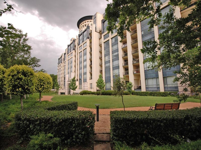 A view of the apartment building exterior featuring a well-maintained landscaped garden, paved walkways, and private balconies overlooking the green space.