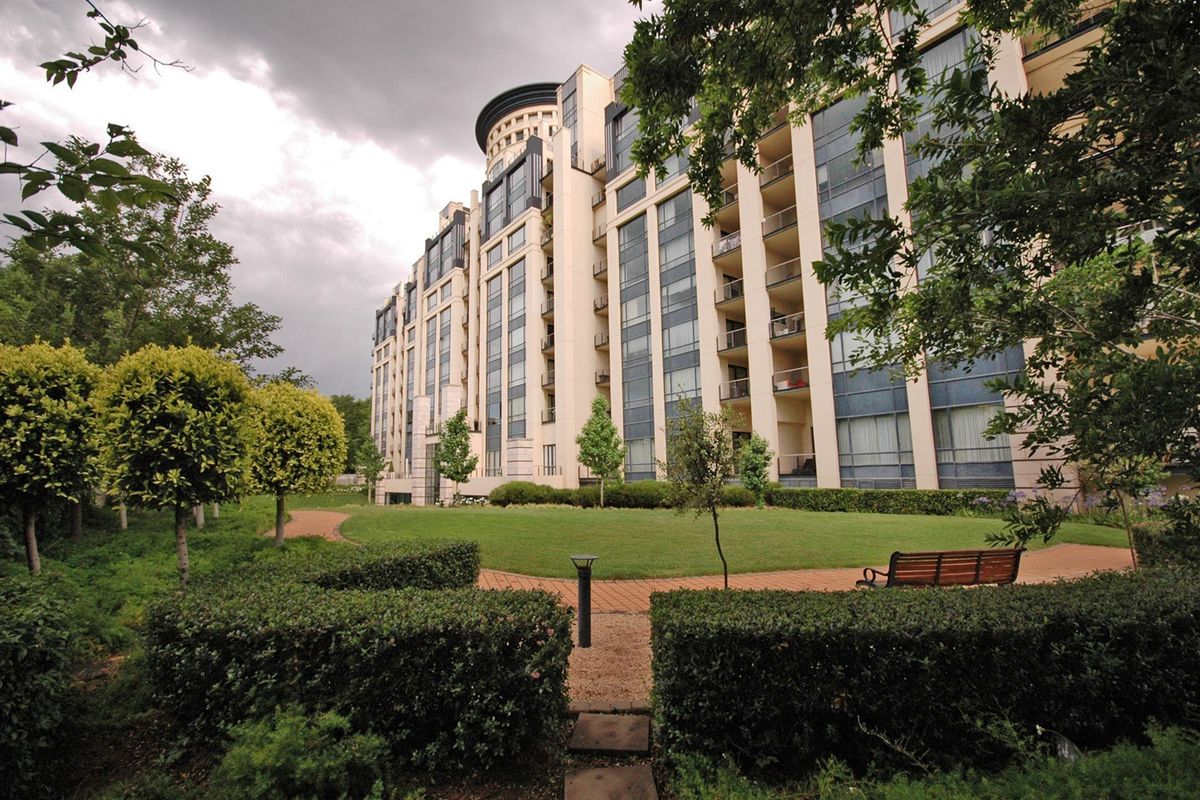 A view of the apartment building exterior featuring a well-maintained landscaped garden, paved walkways, and private balconies overlooking the green space.