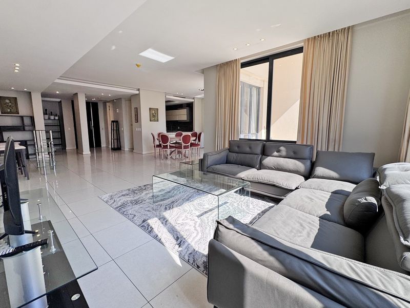 Spacious open-plan living and dining area featuring large format floor tiles, recessed lighting, and seamless flow to the kitchen and outdoor balcony.