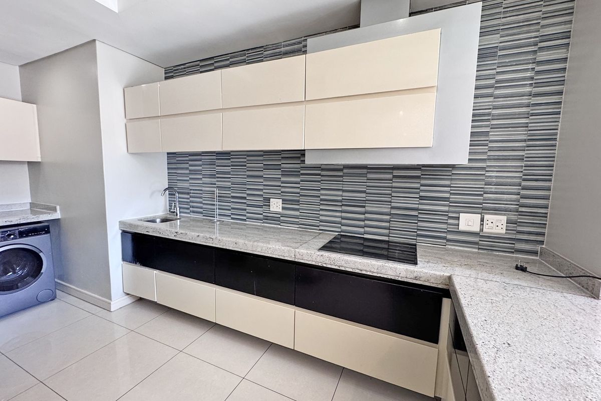 Modern kitchen featuring granite countertops, sleek two-tone cabinetry, integrated electric hob, extractor fan, and tiled backsplash in a clean, contemporary layout.