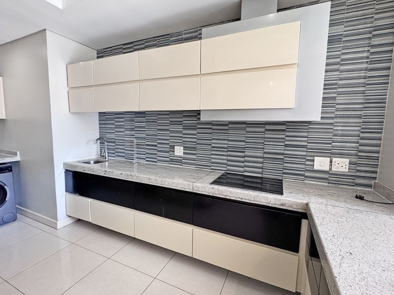 Modern kitchen featuring granite countertops, sleek two-tone cabinetry, integrated electric hob, extractor fan, and tiled backsplash in a clean, contemporary layout.