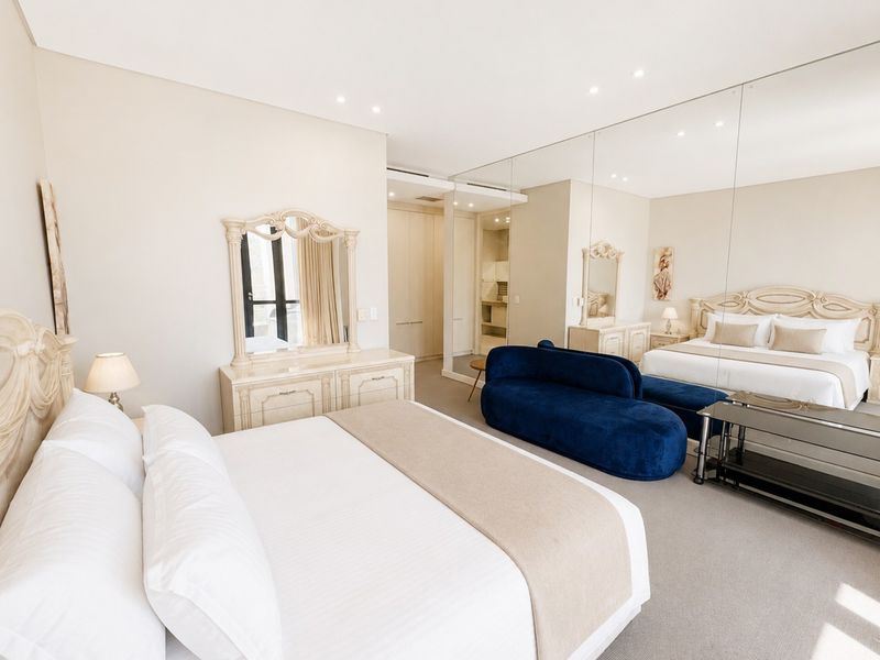 Spacious bedroom featuring neutral tones, built-in cabinetry, recessed lighting, and a large mirrored wall that enhances the sense of space.