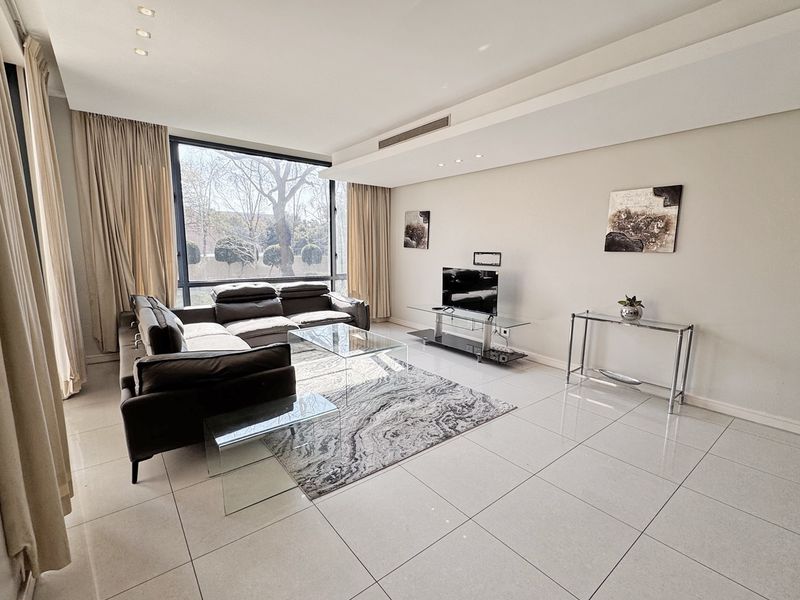 A bright and spacious living room featuring large floor-to-ceiling windows, modern tiled flooring, and recessed ceiling lighting with integrated ducted air conditioning.