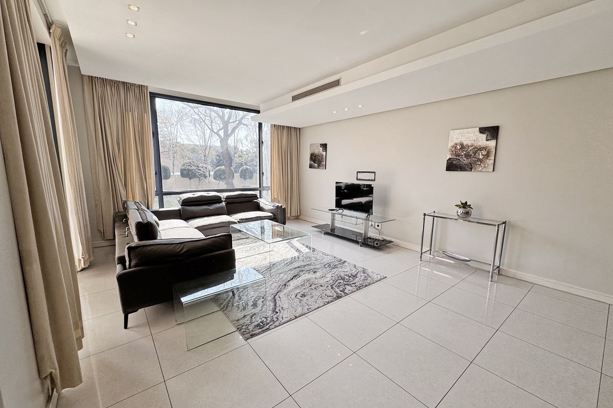 A bright and spacious living room featuring large floor-to-ceiling windows, modern tiled flooring, and recessed ceiling lighting with integrated ducted air conditioning.