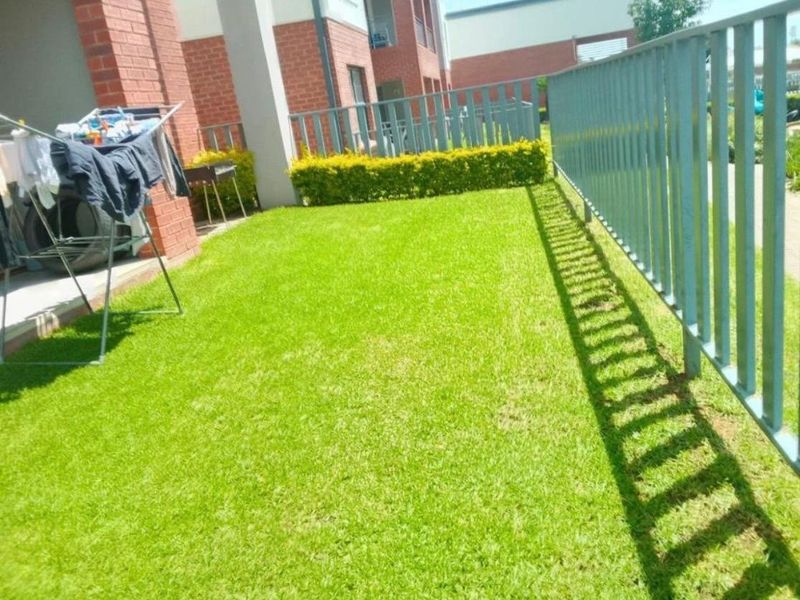A well-maintained private garden area featuring a manicured lawn, neat hedging, and secure metal perimeter fencing adjacent to the apartment building.