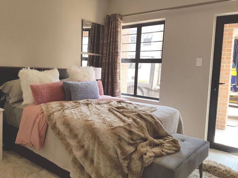 A well-lit bedroom featuring a large window with security bars and a glass door providing direct access to the exterior.