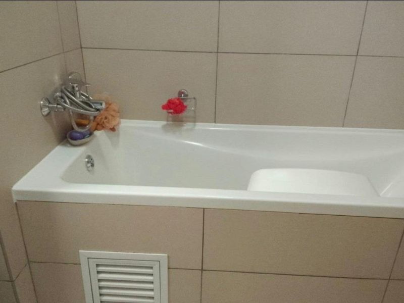 A clean bathroom featuring a built-in bathtub with wall-mounted mixer tap and neutral ceramic wall tiling.