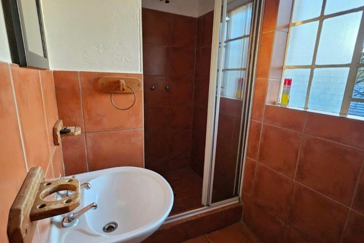 A compact bathroom featuring a pedestal washbasin, a shower enclosure with tiled walls, and a grid window providing natural light.