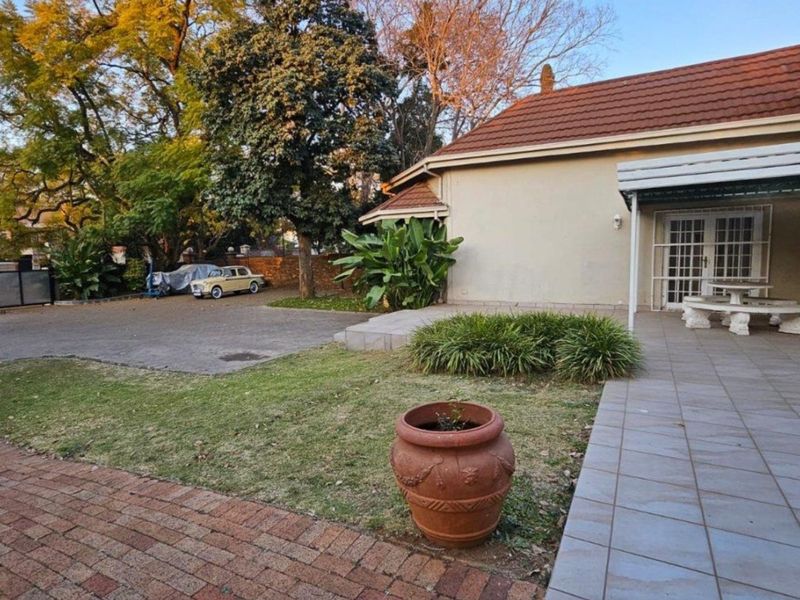 Rear view of the property featuring a tiled patio area, brick paved driveway, and established garden surroundings.