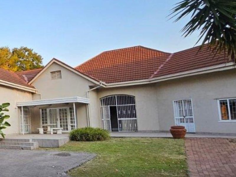 Rear view of the house featuring a tiled roof, security gates, a paved walkway, and a concrete patio area.