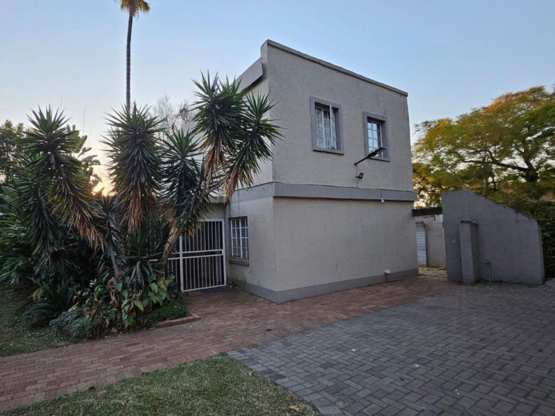 Rear exterior view of a two-story residential property featuring paved driveway, security gates, and established garden landscaping.