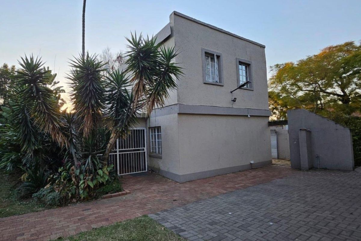 Rear exterior view of a two-story residential property featuring paved driveway, security gates, and established garden landscaping.