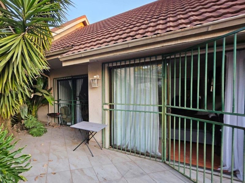 A covered patio area featuring tiled flooring, sliding glass doors with security gates, and direct access to the garden.