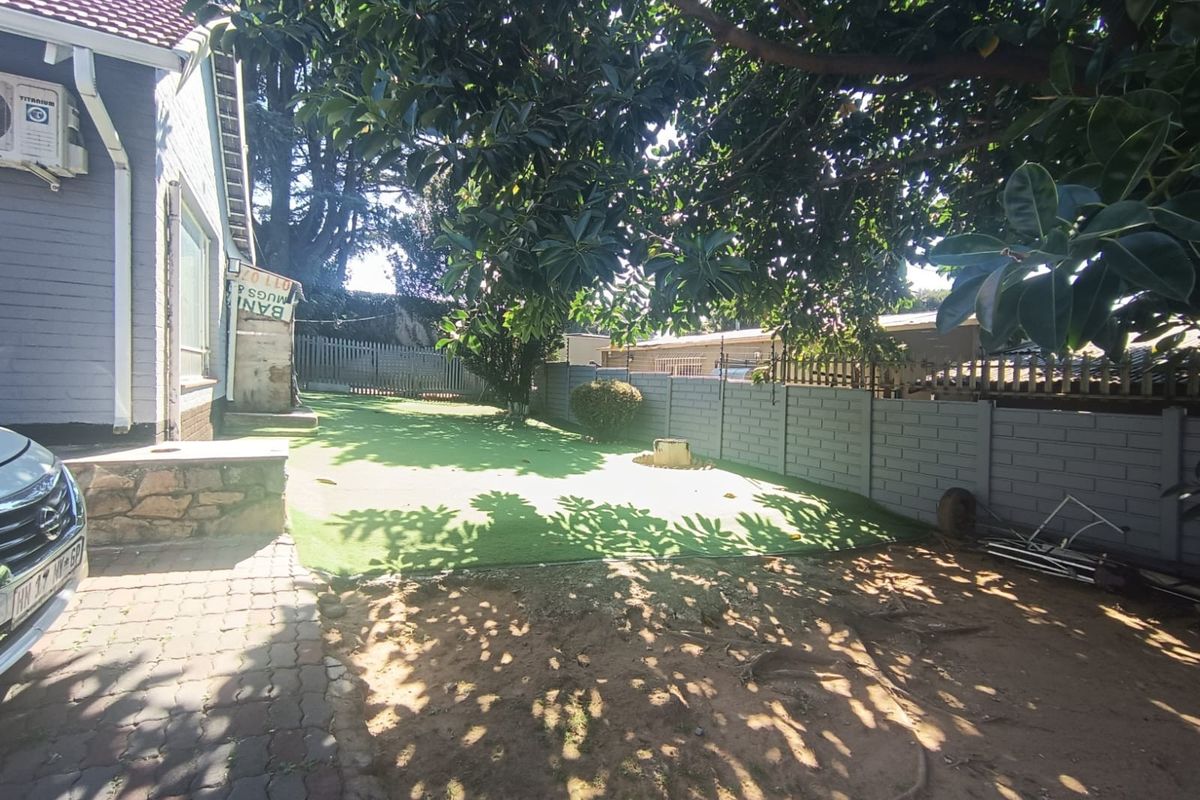 Rear garden area featuring artificial turf, a concrete block boundary wall, and a paved section adjacent to the house exterior.