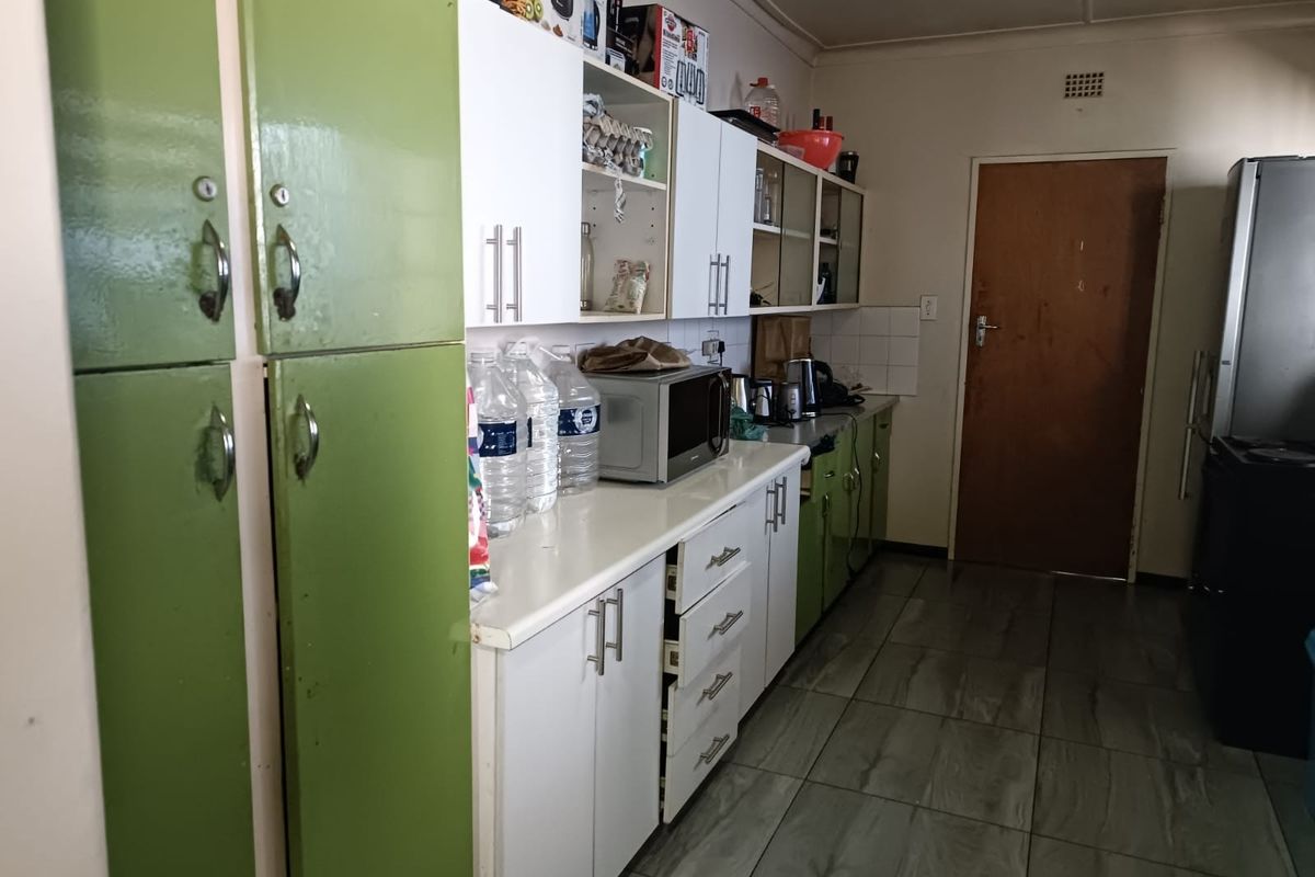 A functional kitchen featuring a mix of green and white cabinetry, laminate countertops, and tiled flooring, offering potential for a modern cosmetic update.