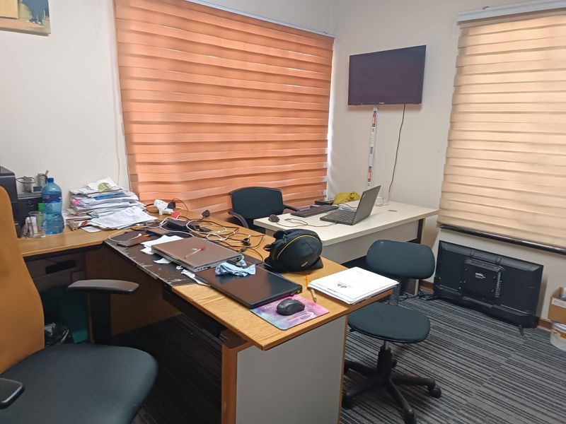 A functional home office space featuring carpeted flooring, dual zebra blinds, and wall-mounted television connectivity.