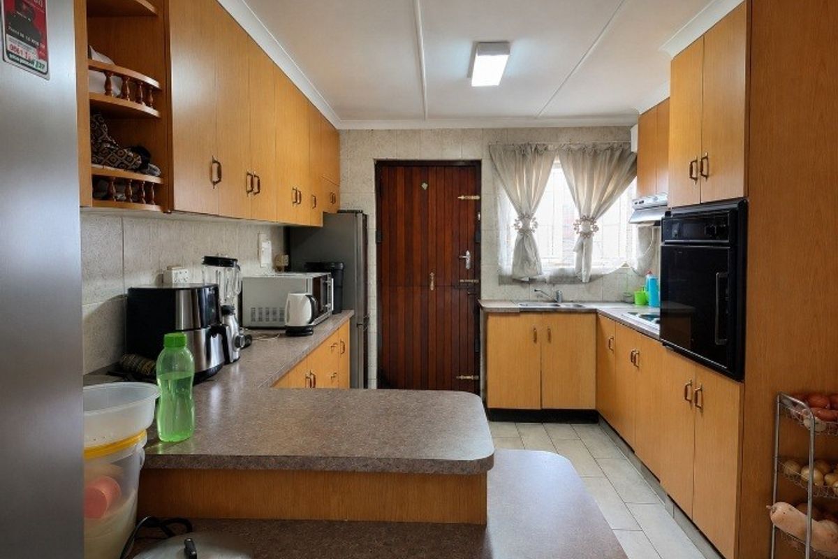 A functional kitchen featuring wood-look laminate cabinetry, built-in oven, extractor fan, and ample countertop space with a practical layout.