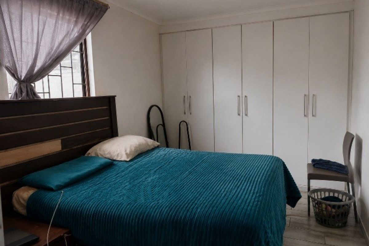 A functional bedroom featuring ample built-in cupboard storage and security bars on the window.