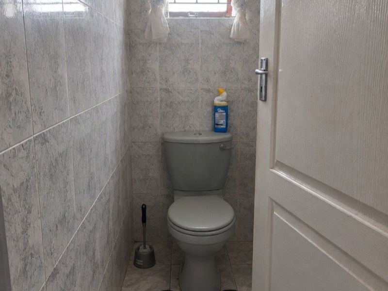 A compact guest bathroom featuring full-height ceramic wall tiling, tiled flooring, and a standard toilet with security bars on the window.