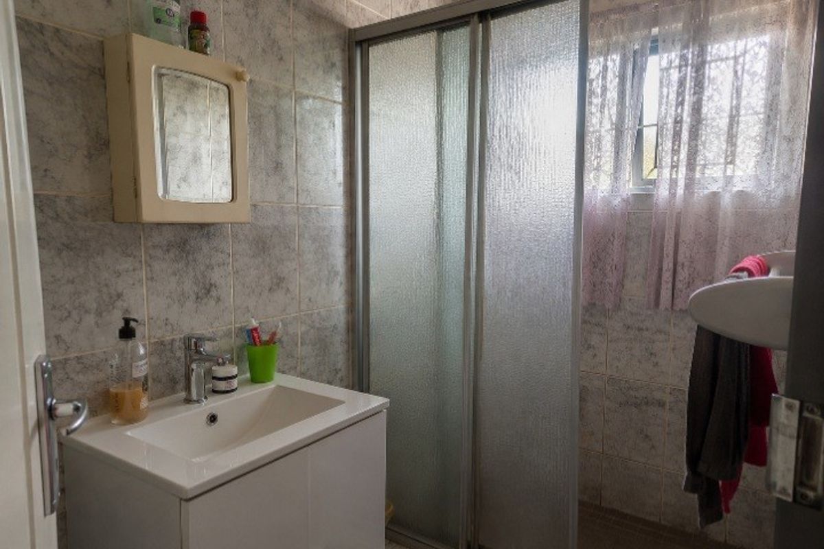 A functional bathroom featuring a vanity basin, a sliding door shower enclosure, and full-height wall tiling with a window for natural light.