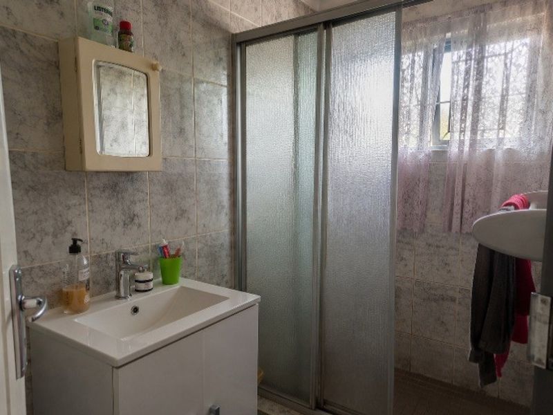 A functional bathroom featuring a vanity basin, a sliding door shower enclosure, and full-height wall tiling with a window for natural light.