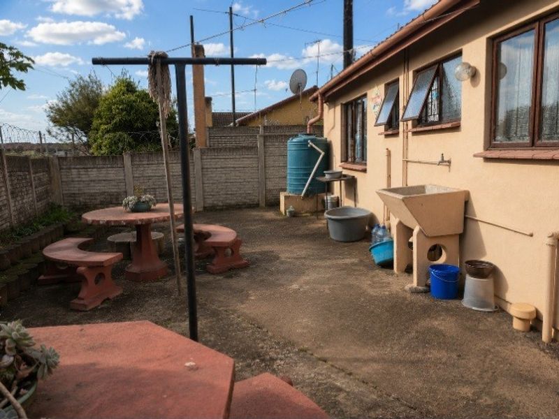 Rear exterior area featuring a concrete patio, brick boundary wall, water tank, and a fixed external laundry sink.