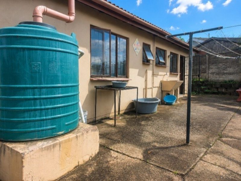 Rear exterior area featuring a water storage tank, concrete wash basin, and paved utility space with a fixed washing line.