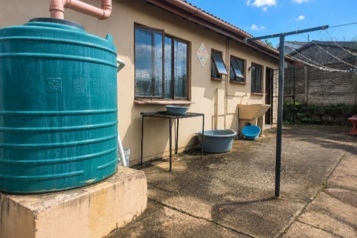 Rear exterior area featuring a water storage tank, concrete wash basin, and paved utility space with a fixed washing line.