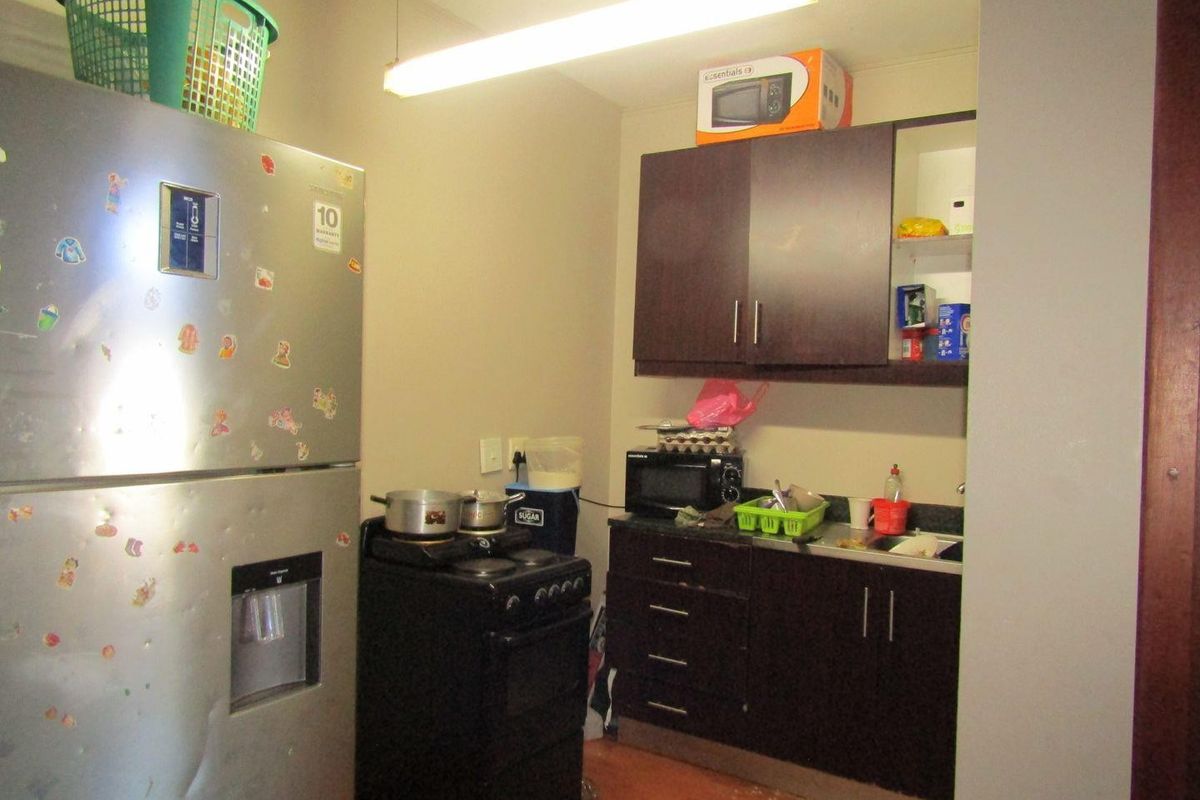 Compact kitchen area featuring dark wood cabinetry, laminate countertops, and a stainless steel sink, requiring cosmetic updates to improve functionality and aesthetic appeal.
