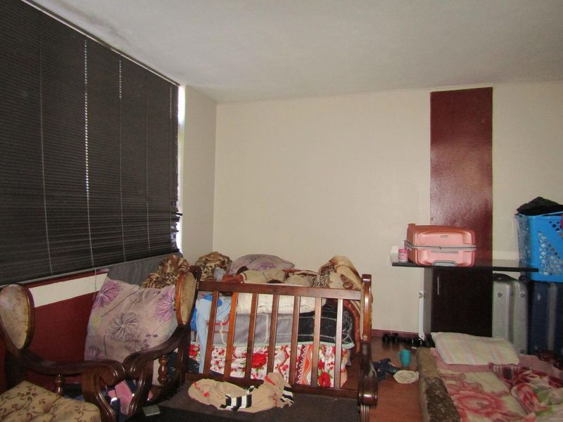A bedroom featuring dark venetian blinds and a built-in shelving unit, requiring cosmetic updates to improve the overall condition and appeal.