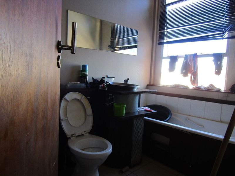 A compact bathroom featuring a toilet, vessel sink vanity, and a bathtub, requiring cosmetic updates to improve its overall condition and appeal.
