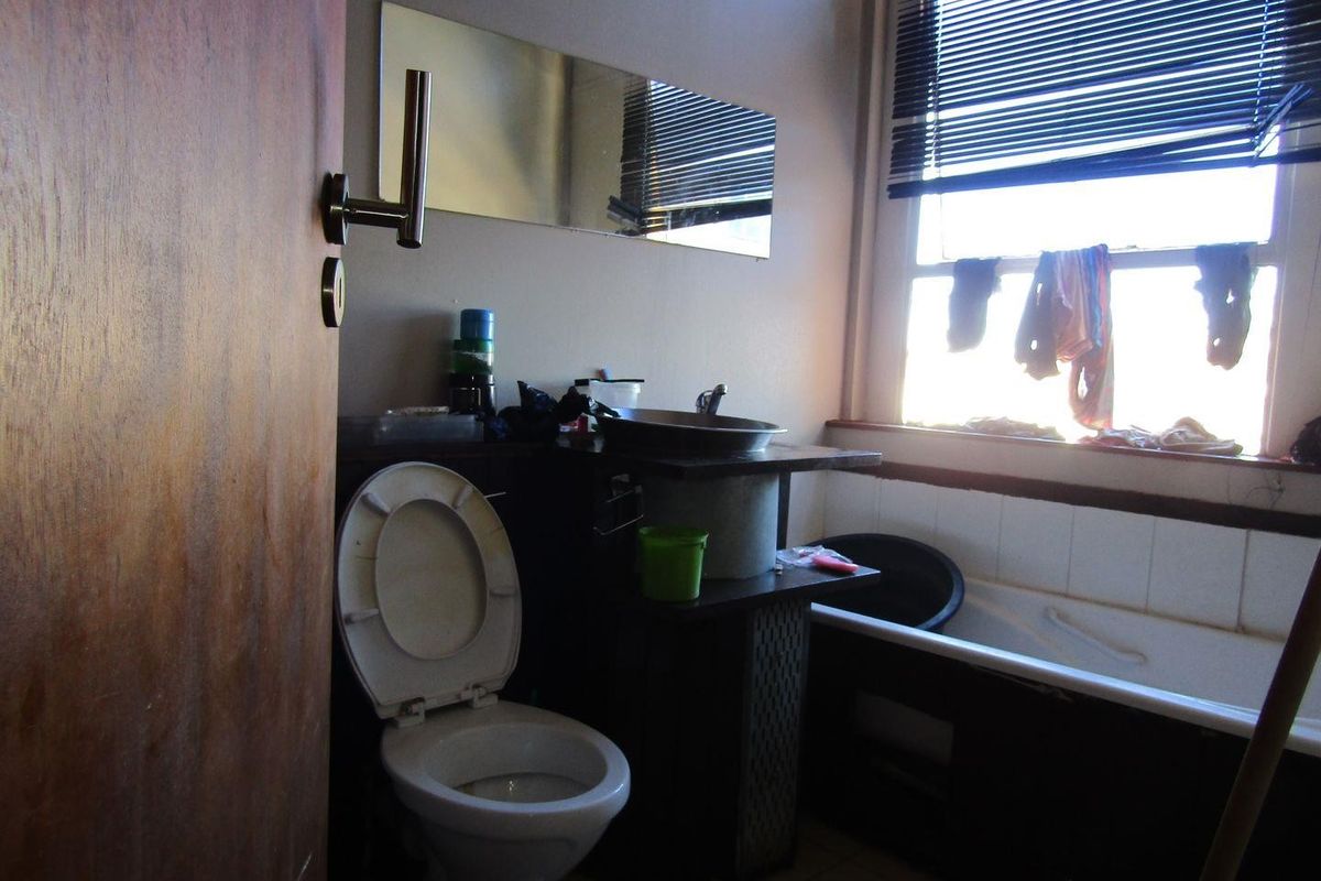 A compact bathroom featuring a toilet, vessel sink vanity, and a bathtub, requiring cosmetic updates to improve its overall condition and appeal.