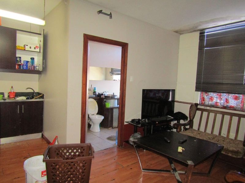 Open plan living area featuring a compact kitchen corner and direct access to the bathroom, with visible wear to flooring and ceiling finishes.