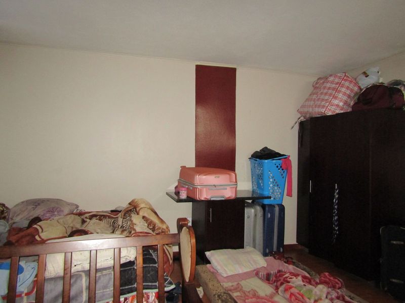 A bedroom interior featuring plain wall finishes and basic structural layout, currently utilized for storage and sleeping.
