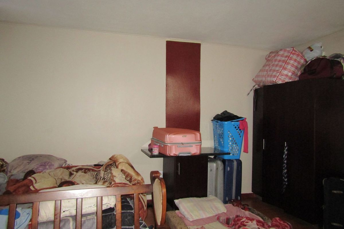 A bedroom interior featuring plain wall finishes and basic structural layout, currently utilized for storage and sleeping.