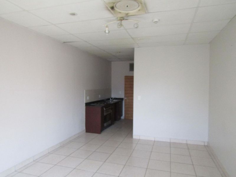 An empty open-plan living and kitchen area featuring tiled floors, built-in cabinetry with integrated appliances, and a drop ceiling in need of maintenance.