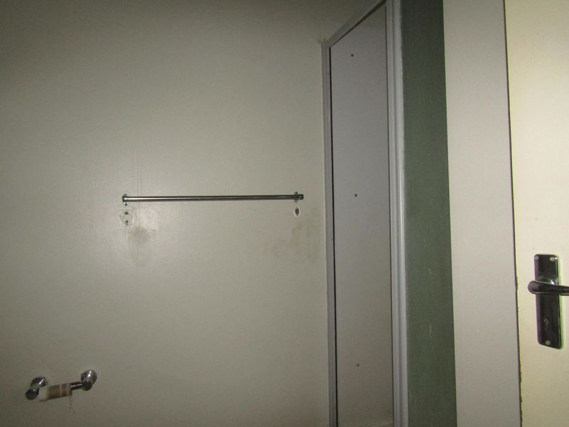 A small bathroom interior featuring a shower enclosure, towel rail, and toilet roll holder, showing signs of wear and wall surface damage.