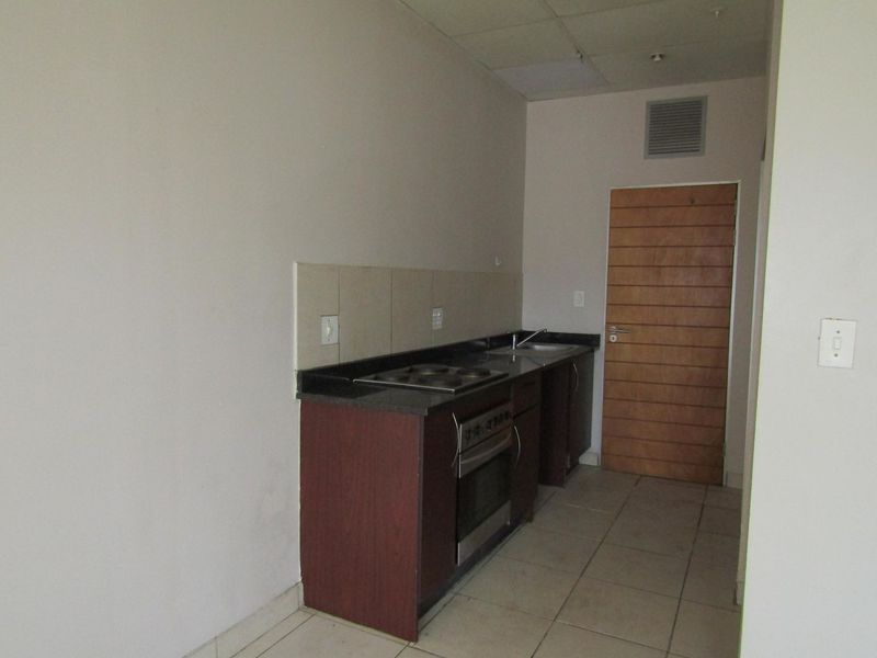 A compact, empty kitchen featuring built-in cabinetry, a stone countertop, integrated oven and hob, and tiled flooring.