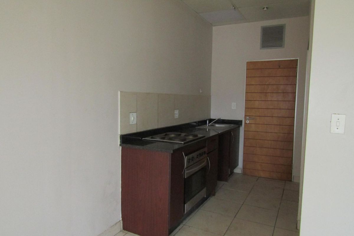 A compact, empty kitchen featuring built-in cabinetry, a stone countertop, integrated oven and hob, and tiled flooring.
