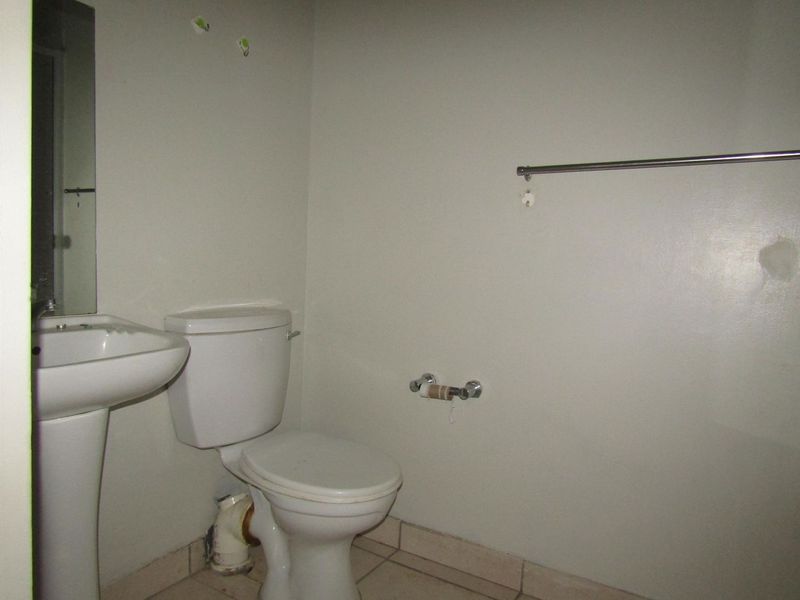 A compact bathroom featuring a pedestal sink, toilet, and tiled flooring, currently requiring cosmetic updates and repairs to wall surfaces and fixtures.